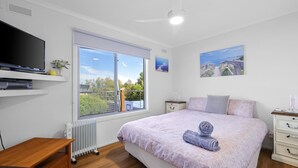 A bedroom with a large window, a bed with rolled towels, a TV, and a painting on the wall. - Family Retreat at Rhyll (Rhyll)