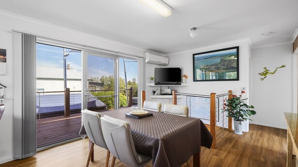 A modern dining area with a table set for two, a television mounted above the table, and a balcony with a view of the surrounding landscape. - Family Retreat at Rhyll (Rhyll)