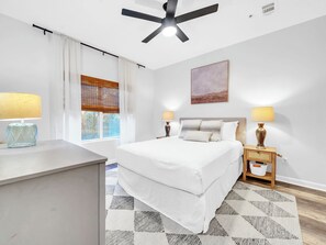 A modern bedroom with a bed, two bedside tables with lamps, a ceiling fan, a window with blinds, and a painting on the wall. - ⭐30A Heron's Watch 1102 | Sugary White Beaches⭐ (Santa Rosa Beach)