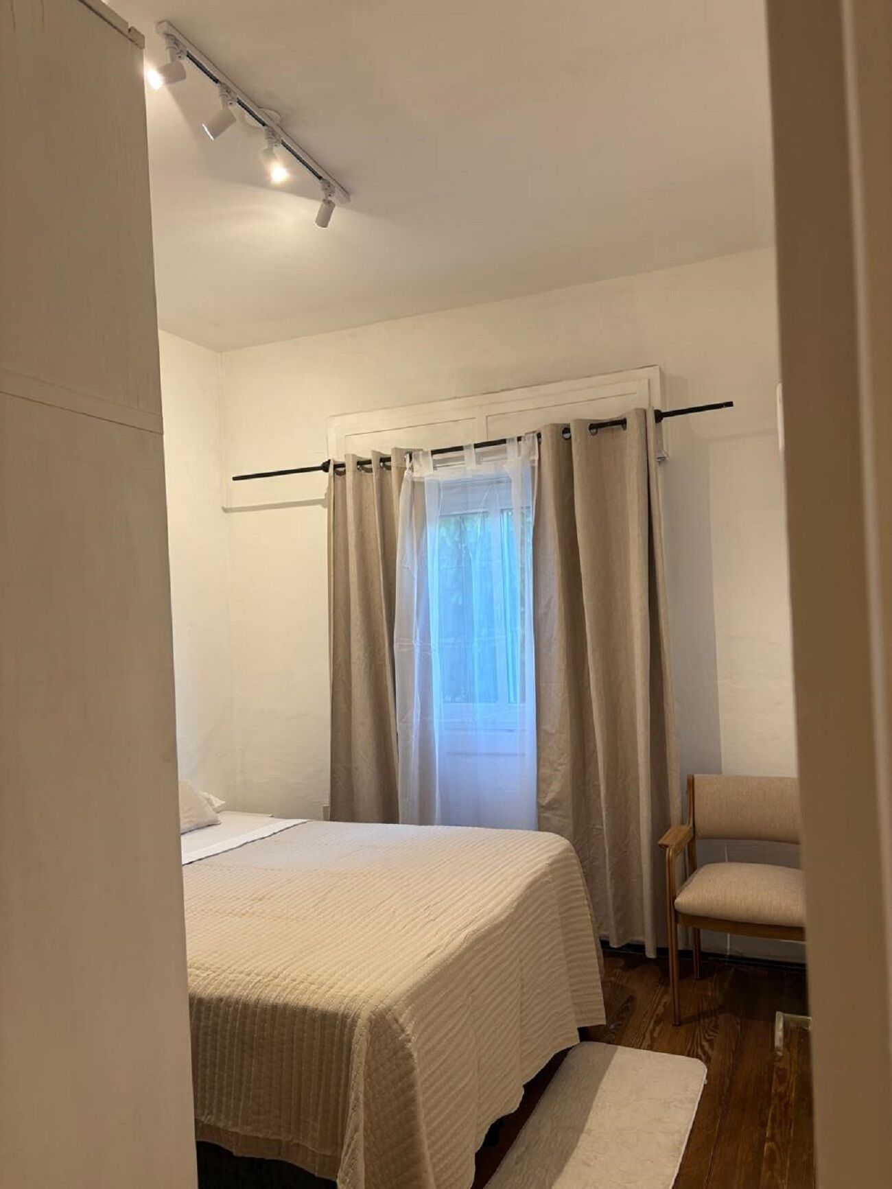 A bedroom with a bed, a chair, a window with curtains, and a ceiling light fixture.