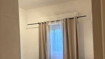 A bedroom with a bed, a chair, a window with curtains, and a ceiling light fixture.