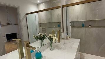 Un baño moderno con tocador blanco, un espejo grande y cabina de ducha de vidrio.