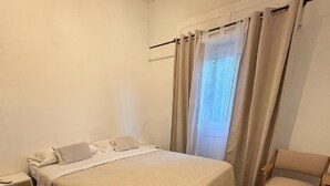 Ein Schlafzimmer mit einem Bett, einem Sessel, einem Nachttisch und einem Fenster mit Vorhängen.