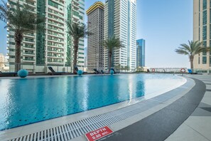 A swimming pool with a depth sign, surrounded by tall buildings and palm trees. - Stayshort - Contemporary 1BR Escape for 4 in Dubai Marina (Dubai)