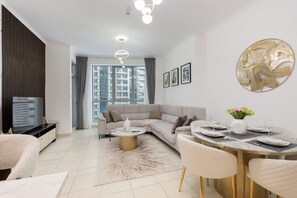 A modern living room with a sectional sofa, a round dining table, and a large window with a view of high-rise buildings. - Stayshort - Contemporary 1BR Escape for 4 in Dubai Marina (Dubai)