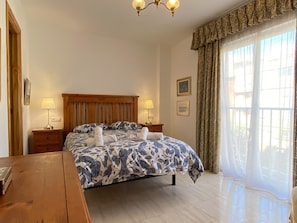 A hotel room with a bed, bedside lamps, a wooden nightstand, a wooden dresser, and a large window with curtains. - Apartment in Nerja Near Sandy Beach (Nerja)