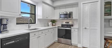 A modern kitchen with white cabinetry, stainless steel appliances, and a built-in oven.