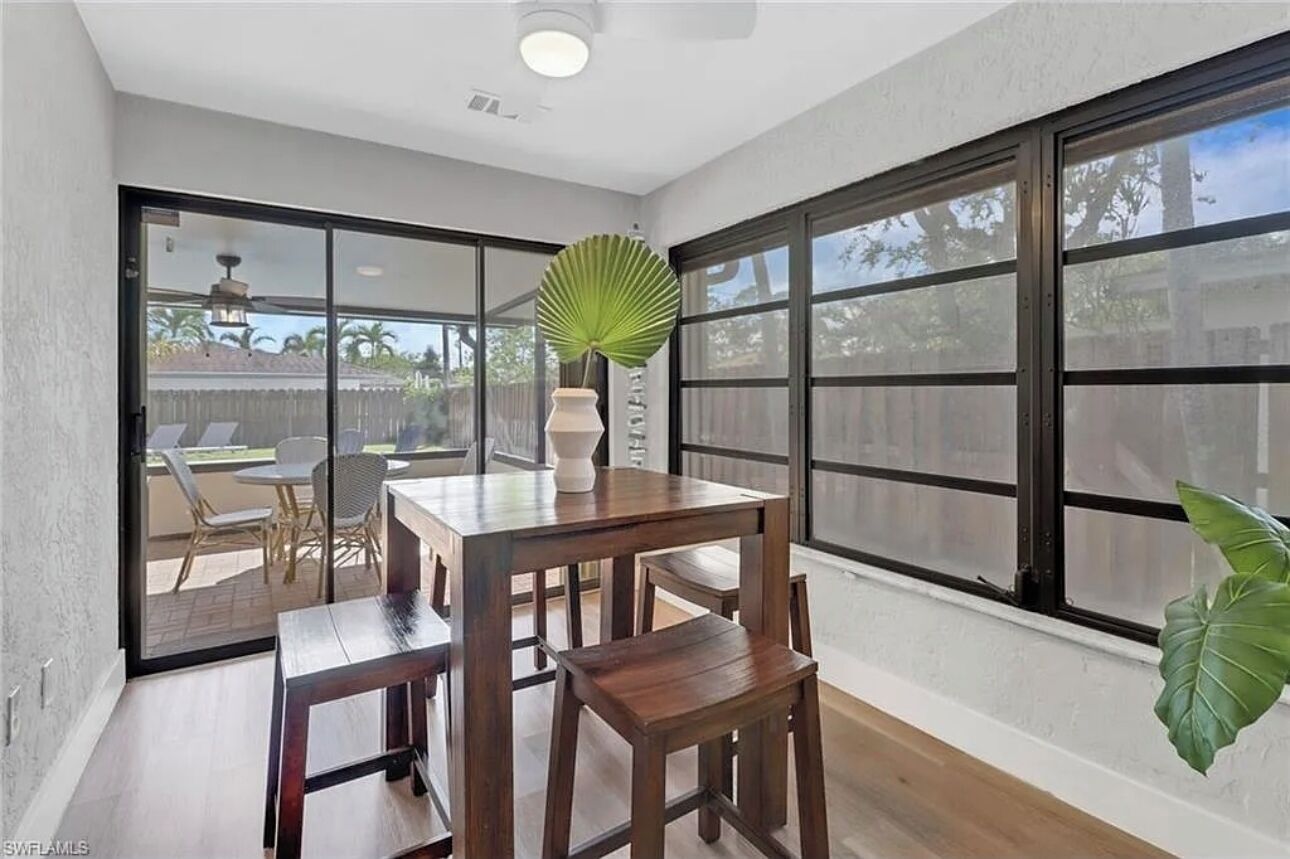 A dining area with a table and chairs, large windows, and a view of the backyard.