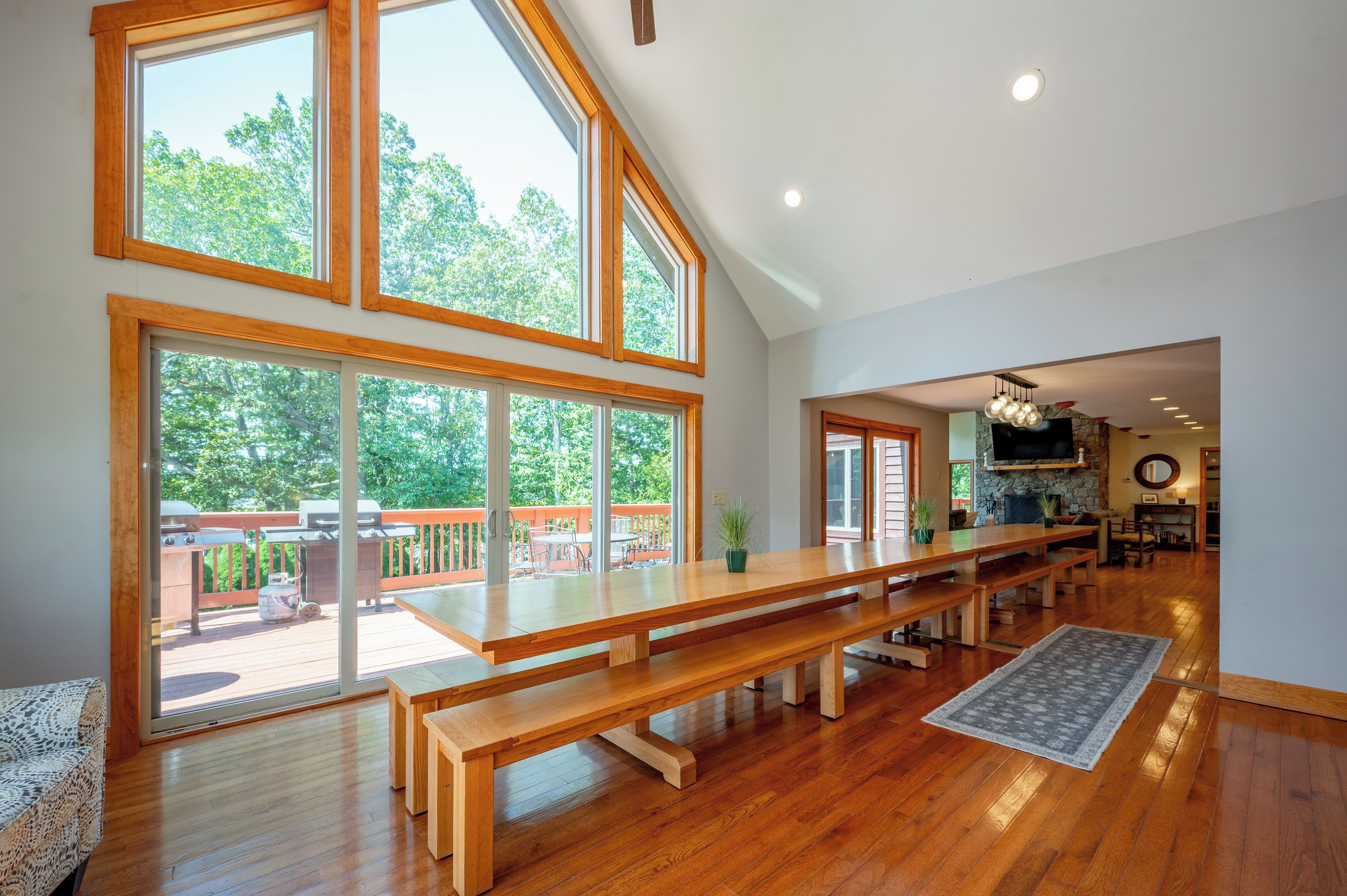 A spacious interior with a large wooden dining table, multiple benches, and a view of a deck with outdoor furniture.