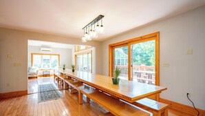 A spacious room with a long wooden table, benches, and large windows offering a view of the outdoors. - Dog Friendly Lakefront Home w/ Pool & Hot Tub! (Swanton)