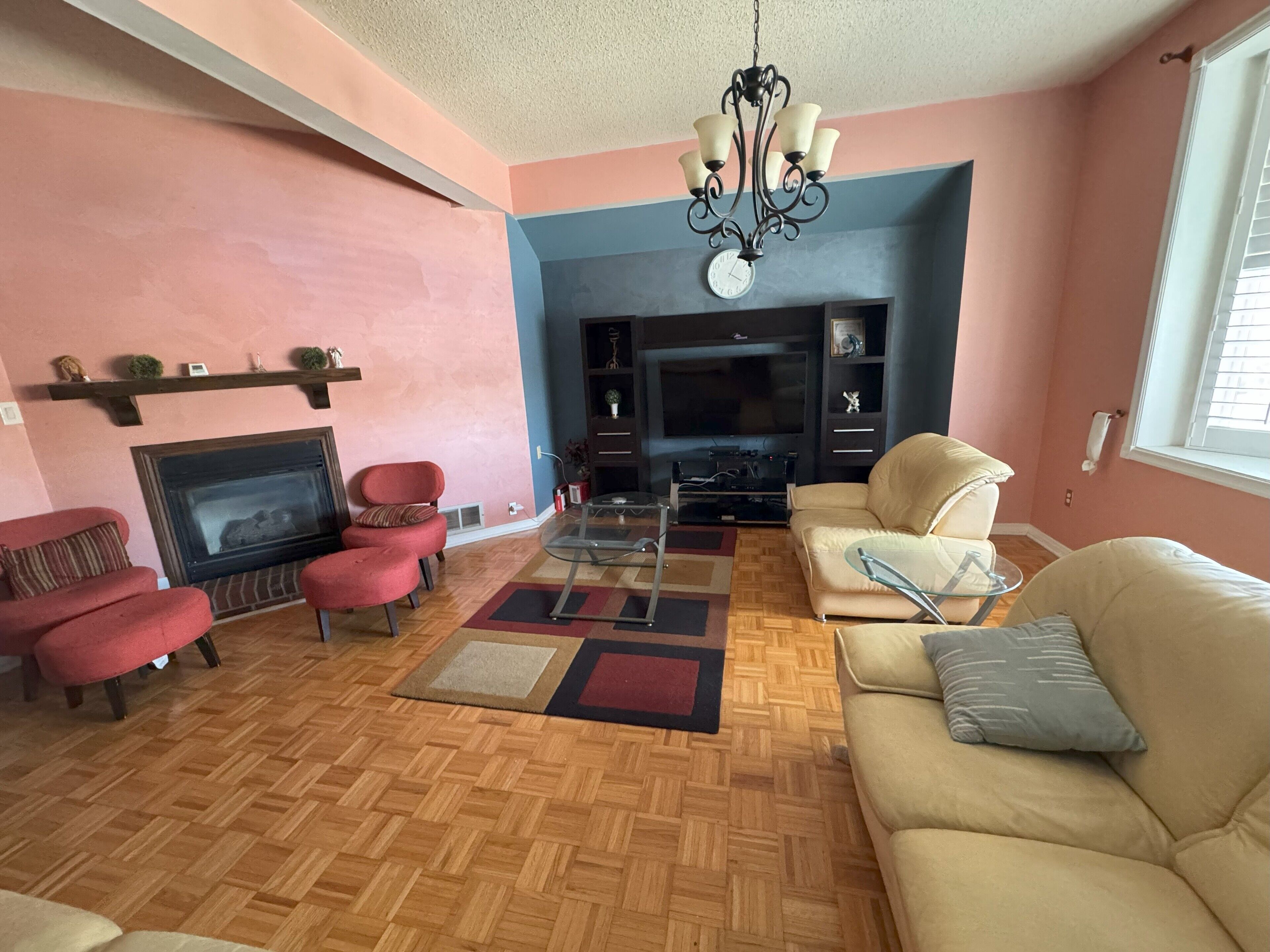 A living room with a fireplace, red and beige sofas, a TV, and a chandelier.