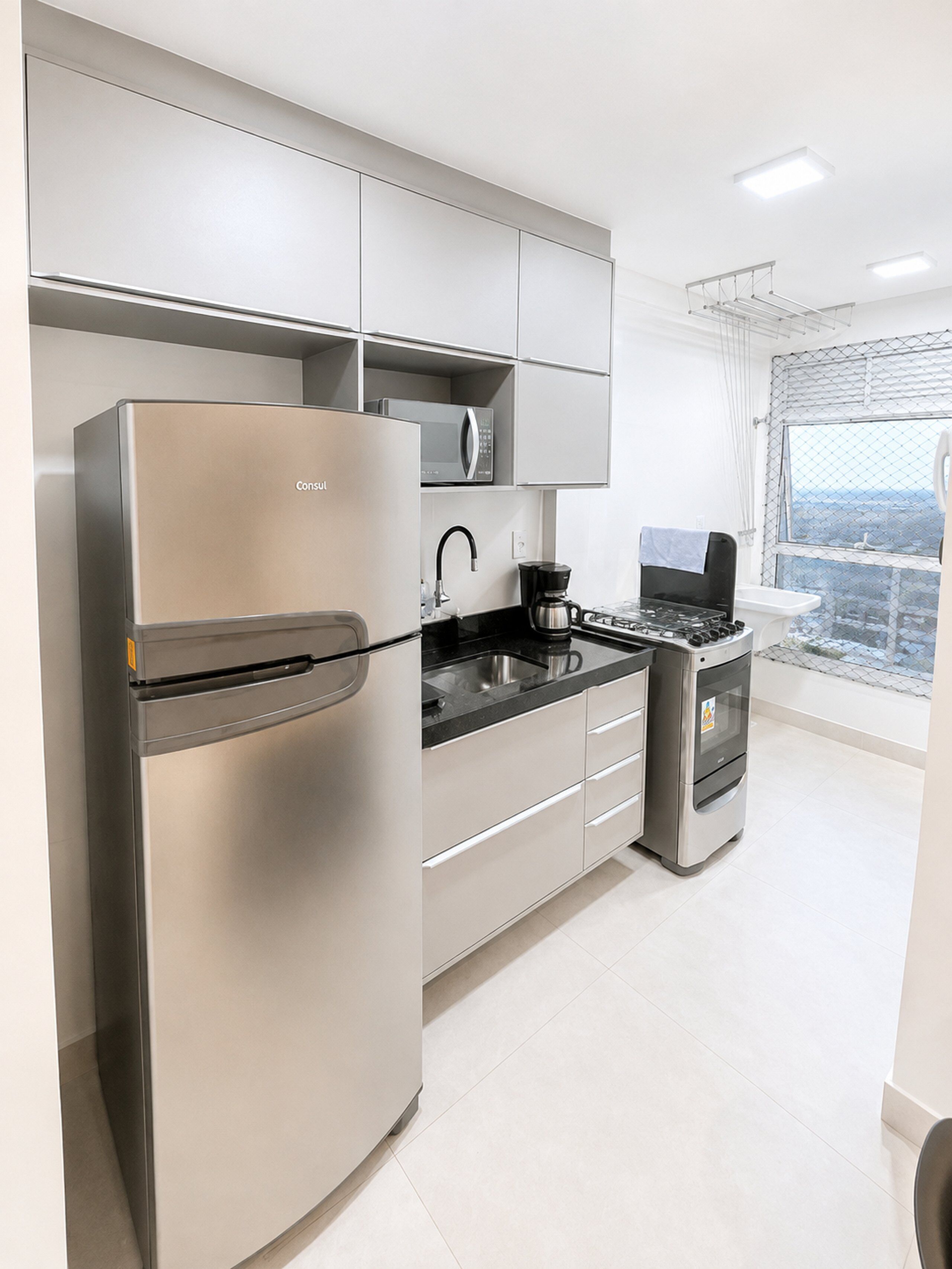 Cozinha moderna com eletrodomésticos de aço inoxidável, bancada preta e vista pela janela.