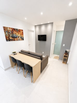 A modern living space with a dining area, a sofa, a flat-screen TV, and a painting on the wall. - Edifício Infinity by Housi (Vila Velha)