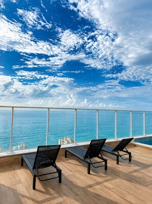 A deck with two lounge chairs facing a large window overlooking the sea. - Edifício Infinity by Housi (Vila Velha)
