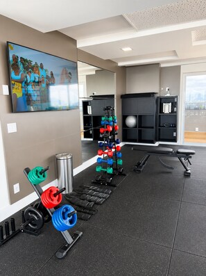 A gym with weightlifting equipment, a bench, and a painting on the wall.