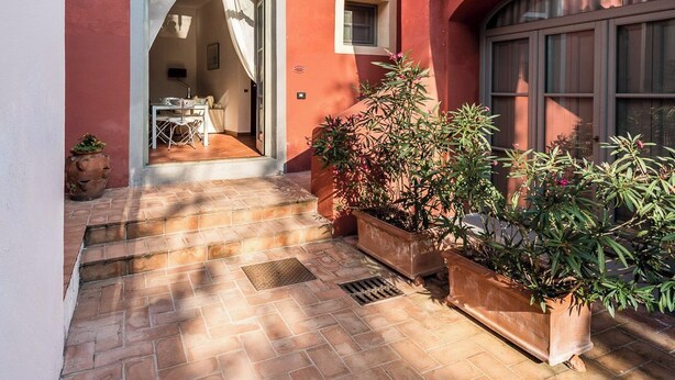 A red building with a tiled courtyard, a door leading to a room, and potted plants. - Superior Apartment Borgo di Matraia (Matraia)