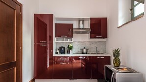 A compact kitchen with dark red cabinets, a stainless steel range hood, and a microwave on the countertop. - Superior Apartment Borgo di Matraia (Matraia)