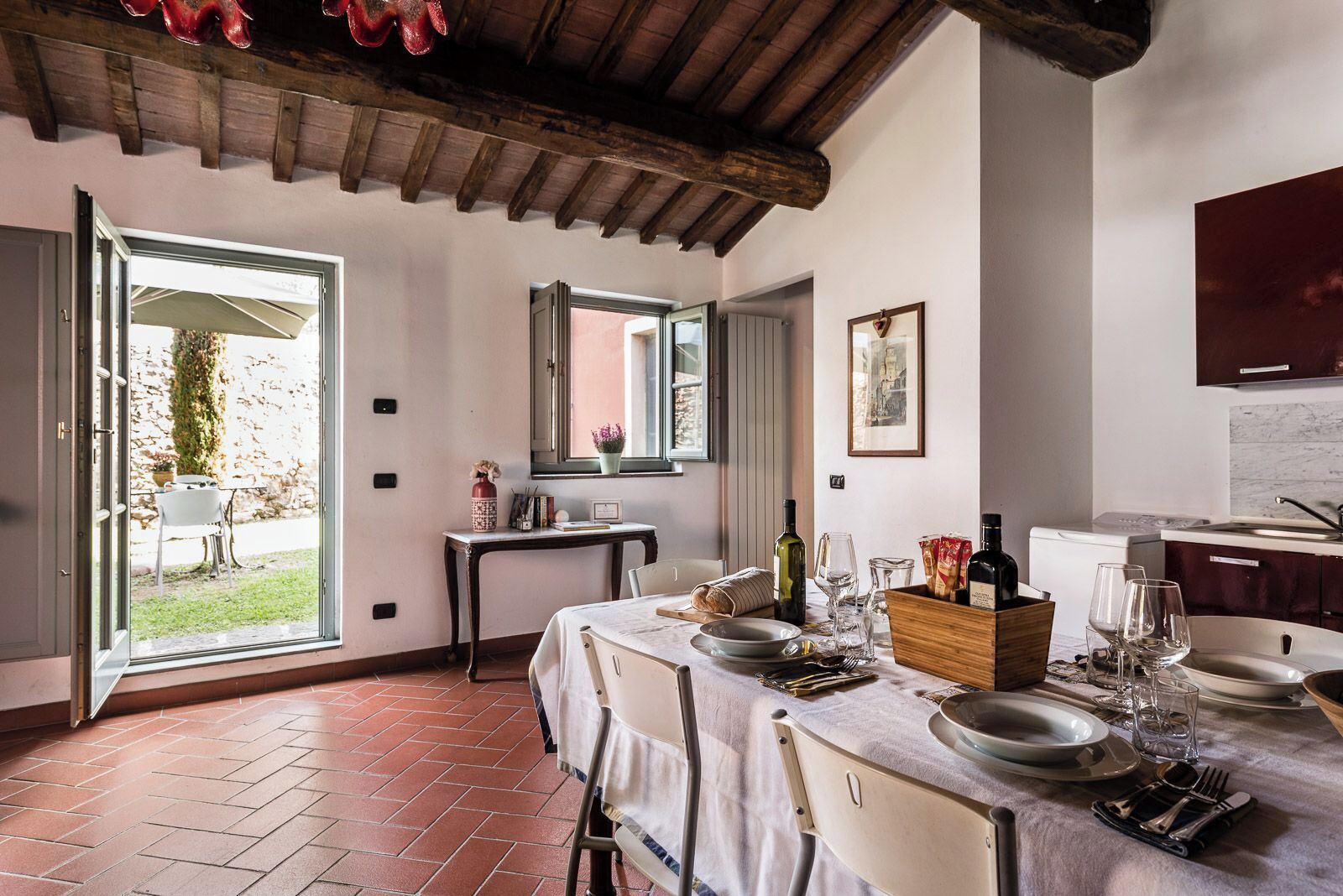 A dining area with a table set for four, a kitchen in the background, and a view of the outdoors through an open door.