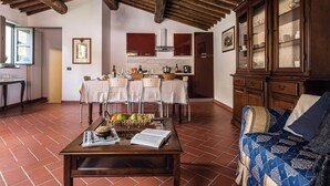 A dining area with a table set for four, a kitchen with wooden cabinets, and a living area with a sofa and patterned cushions. - Superior Apartment Borgo di Matraia (Matraia)
