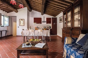 Un comedor con una mesa dispuesta para cuatro, una cocina con armarios de madera y una sala de estar con un sofá y cojines estampados.