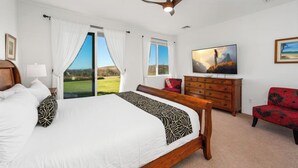 A bedroom with a large bed, a wooden dresser, a red chair, a ceiling fan, and a TV on the wall. - Newly Remodeled Home in Waikoloa Village!  WeloWelo House (Waikoloa Village)