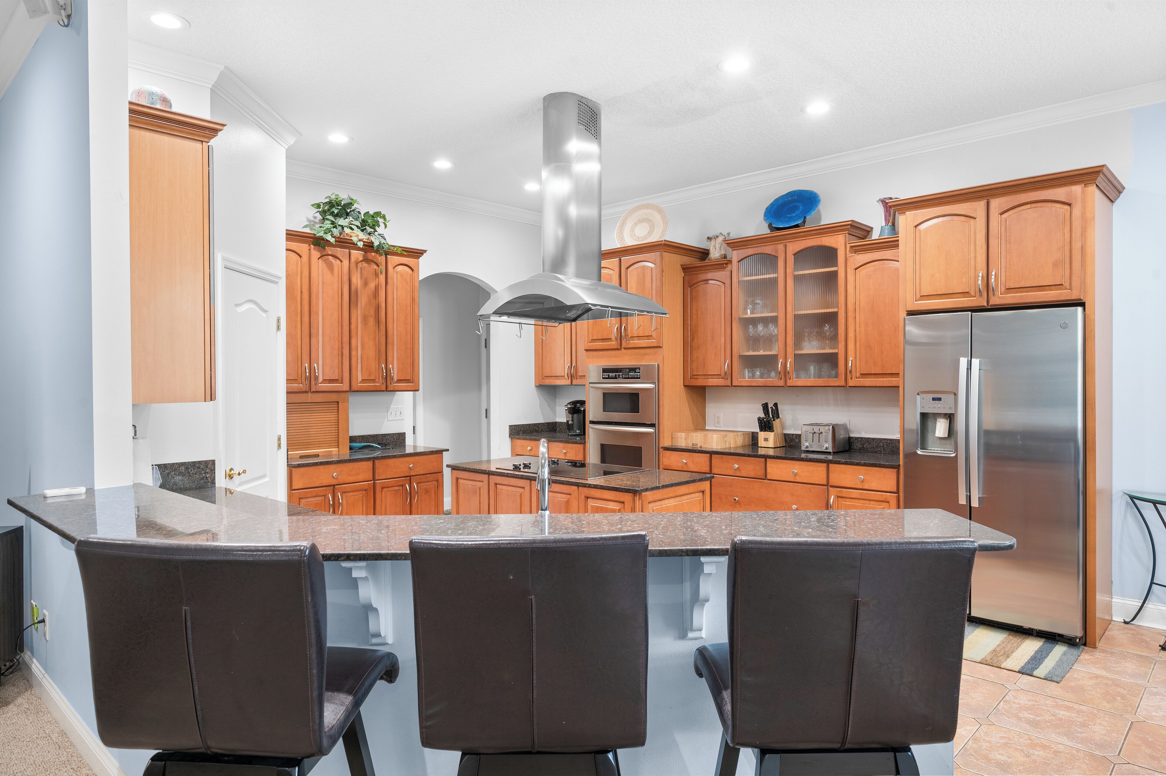 Une cuisine moderne avec des meubles en bois, des appareils électroménagers en acier inoxydable et un îlot central doté de tabourets de bar.