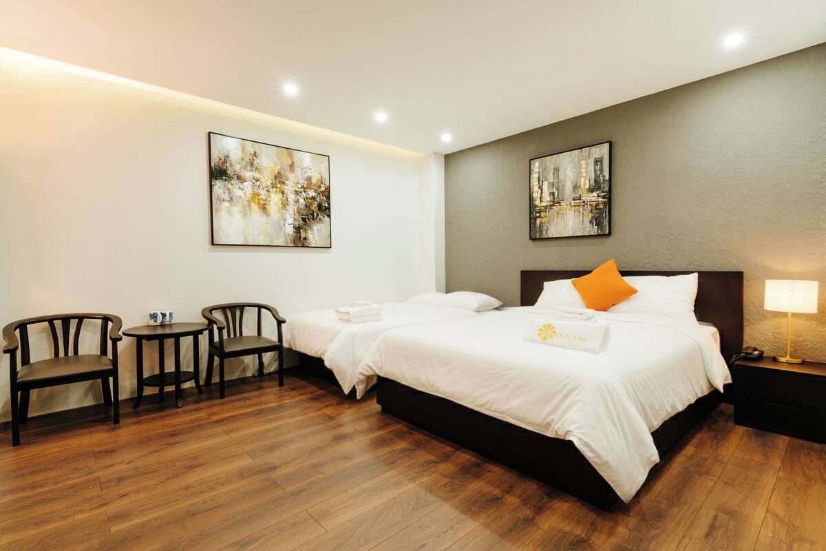 Habitación de hotel con dos camas, una mesita, dos sillas y obras de arte en las paredes.