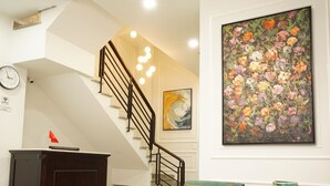 Un vestíbulo de hotel con una escalera, un cuadro floral grande, un reloj y una mesa de recepción.