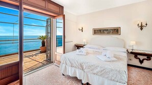 Ein Hotelzimmer mit einem großen Bett, Meerblick, einer Topfpflanze und einem Gemälde an der Wand.