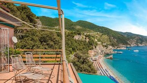 Eine Terrasse mit Sitzgelegenheiten und Blick auf eine Küstenlandschaft mit Gebäuden und Strand.