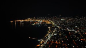Vue aérienne d’une ville côtière de nuit, avec des rues illuminées et un pont imposant.
