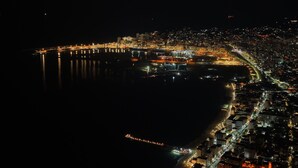 Vue aérienne d’une ville côtière de nuit, avec ses rues et ses bâtiments illuminés le long du front de mer.