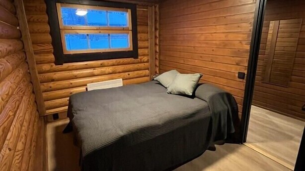 Quarto de cabana de tronco com cama, janela e porta.