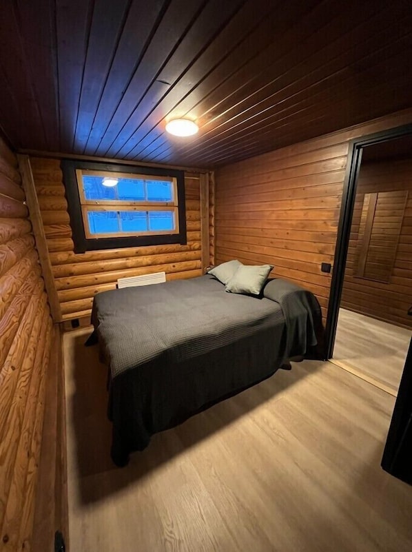 A log cabin bedroom with a bed, a window, and a door.