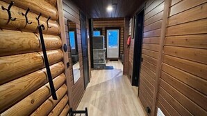 Um interior de madeira com um banco, um cabide e uma porta que dá para outro cômodo.