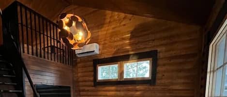 A log cabin interior with a staircase, a sofa, a hanging light fixture, and a window.