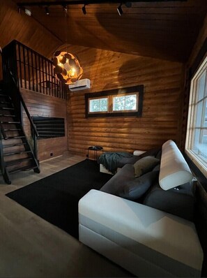 Een vakantiehuisje van binnen met een trap, een bank, een hanglamp en een raam.