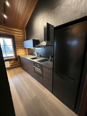 Een moderne keuken met een zwarte koelkast, roestvrijstalen apparatuur en houten lambrisering.