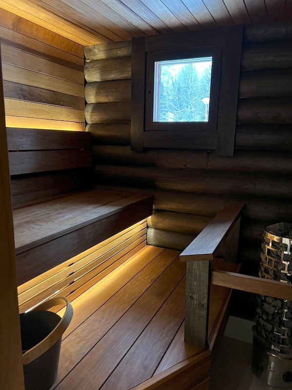 A log cabin interior with a wooden bench, a small window, and a stone fireplace.