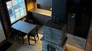 A cozy cabin interior with a stone fireplace, wooden walls, a dining area, and a kitchen with dark cabinetry. - Cottage Lomahimos 18 (Jämsä)