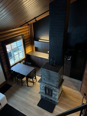 A cozy cabin interior with a stone fireplace, wooden walls, a dining area, and a kitchen with dark cabinetry. - Cottage Lomahimos 18 (Jämsä)