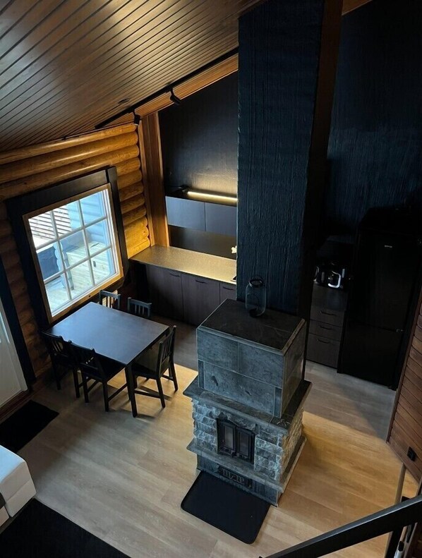 A cozy cabin interior with a stone fireplace, wooden walls, a dining area, and a kitchen with dark cabinetry.