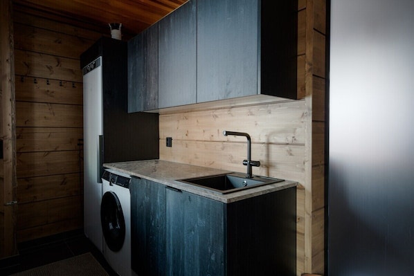 A compact kitchen with a washing machine, a sink, and wooden walls.