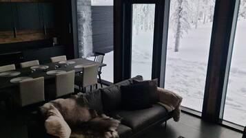 Moderni olohuone, jossa on suuri ikkuna, nahkasohva, lasinen sohvapöytä ja koristeellinen kattokruunu.