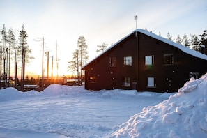 A wooden cabin with a sloped roof, surrounded by snow and trees.