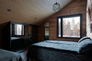 A cabin bedroom with a sloped ceiling, a large window, and a bed with a quilted cover. - Levi utsuvaara frame b (Sirkka)