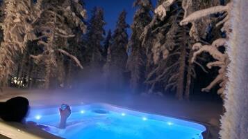 A hot tub surrounded by snow-covered trees at night.