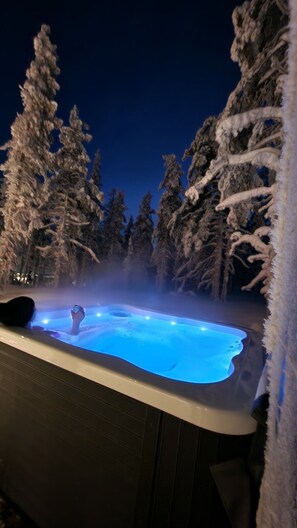 A hot tub surrounded by snow-covered trees at night. - Levi utsuvaara frame b (Sirkka)