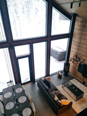 A modern interior with large windows, a fireplace, a sofa, and a dining table.