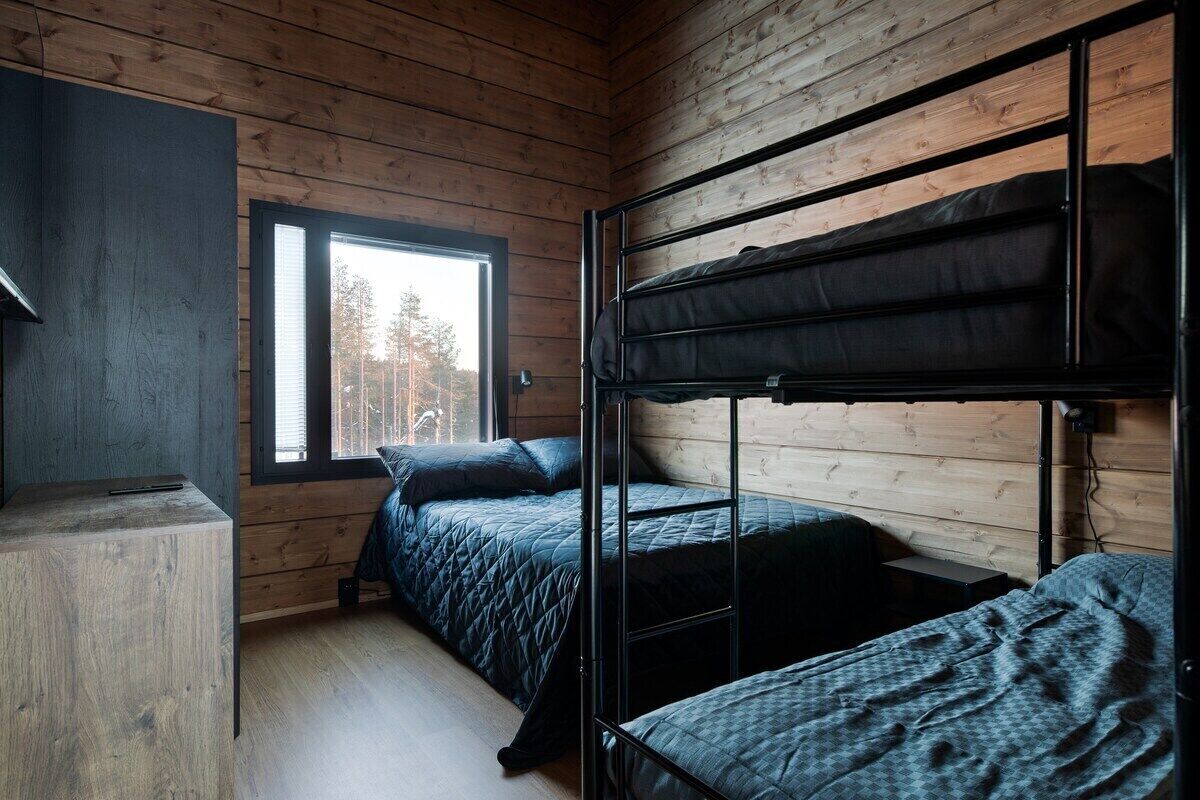 Huoneessa on puuseinät, kerrossänky, työpöytä ja ikkuna, josta avautuu näkymä puihin.